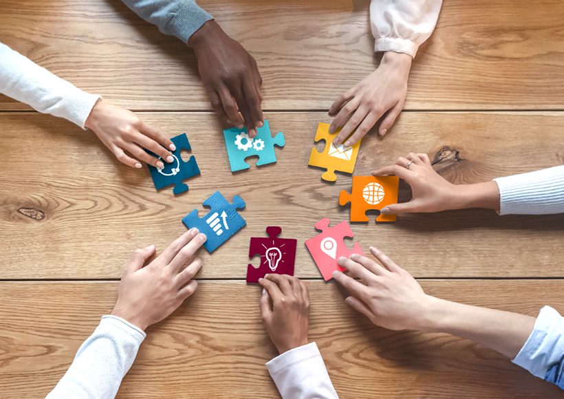 Hands of international coworkers putting colorful puzzles together